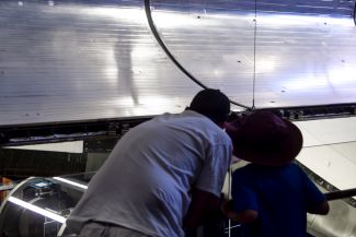Kai and Kenny, near the edge of the left payload bay door with its shiny metal heat radiator retracted back against the inside surface of the door, with the leading portion of the left wing beneath it, to the right.